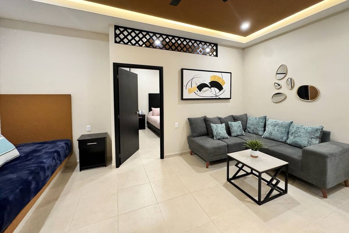A modern living room with a sofa, a coffee table, a bed, and a ceiling fan.