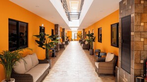 A corridor with a high ceiling, bright lighting, and a central walkway flanked by seating areas and potted plants. - HOTEL SOCRAM GH  (Cabo San Lucas)