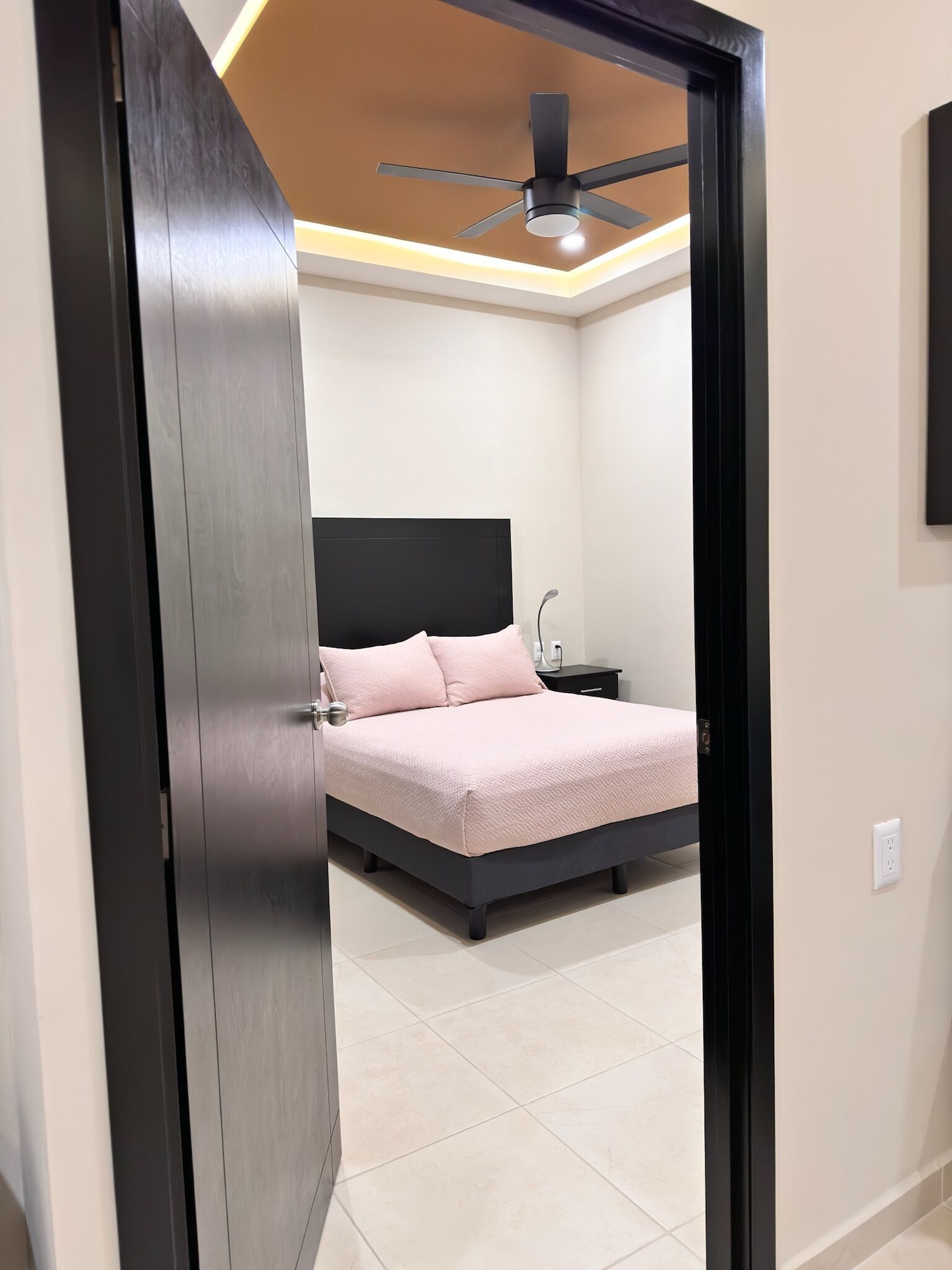 A bedroom with a bed, a nightstand, a ceiling fan, and a door.
