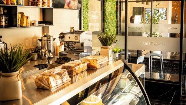 A bakery counter with pastries and a display case, a coffee machine, and hanging pendant lights. - HOTEL SOCRAM GH  (Cabo San Lucas)