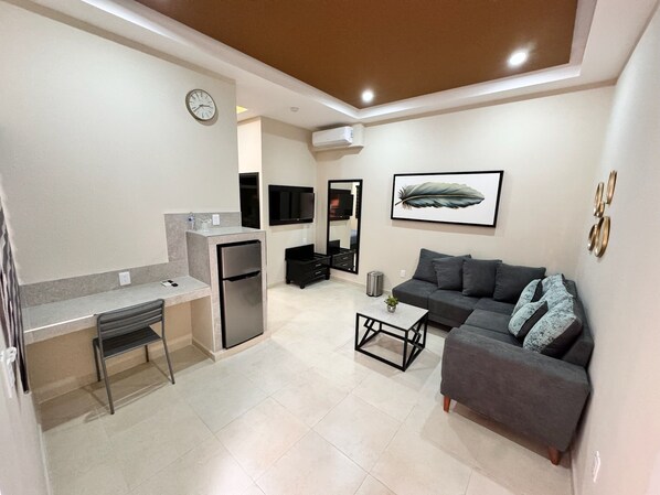 Un salon moderne avec un canapé gris, une petite table basse et un téléviseur fixé au mur.