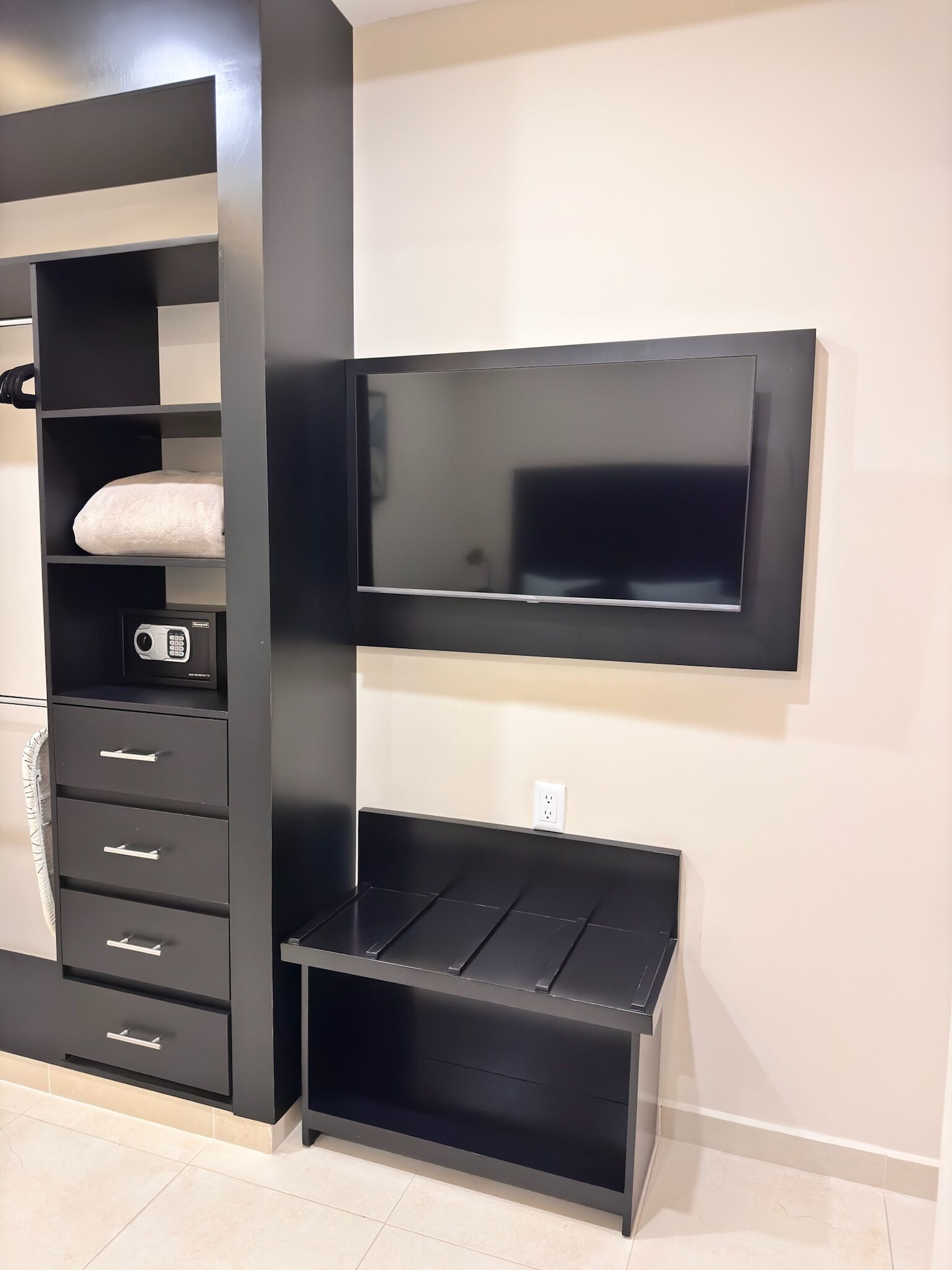 A modern room with a built-in TV, a black entertainment unit with drawers, and a small seating area.