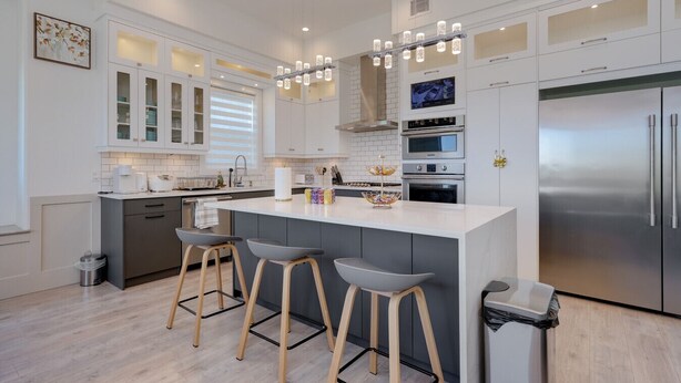 A modern kitchen with white cabinetry, stainless steel appliances, and a central island with bar stools. - Marvelous Home In Victoria, BC (Langford)