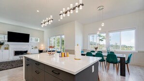 A modern kitchen with a large island, a dining area with green chairs, and a fireplace. - Marvelous Home In Victoria, BC (Langford)