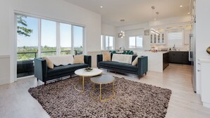 A spacious living area with two dark sofas, a round coffee table, and a large window offering a view of greenery. - Marvelous Home In Victoria, BC (Langford)