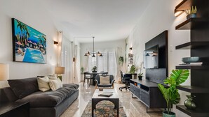 Un soggiorno moderno con un divano scuro, un tavolino, una TV e un'area pranzo con tavolo e sedie.