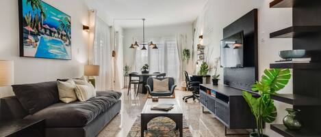 Una sala de estar moderna con un sofá oscuro, una mesa de centro, un televisor y un comedor con una mesa y sillas.