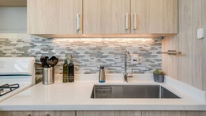 Una cucina moderna con mobili chiari in legno, un lavello in acciaio inossidabile e una parete di fondo rivestita di piastrelle.