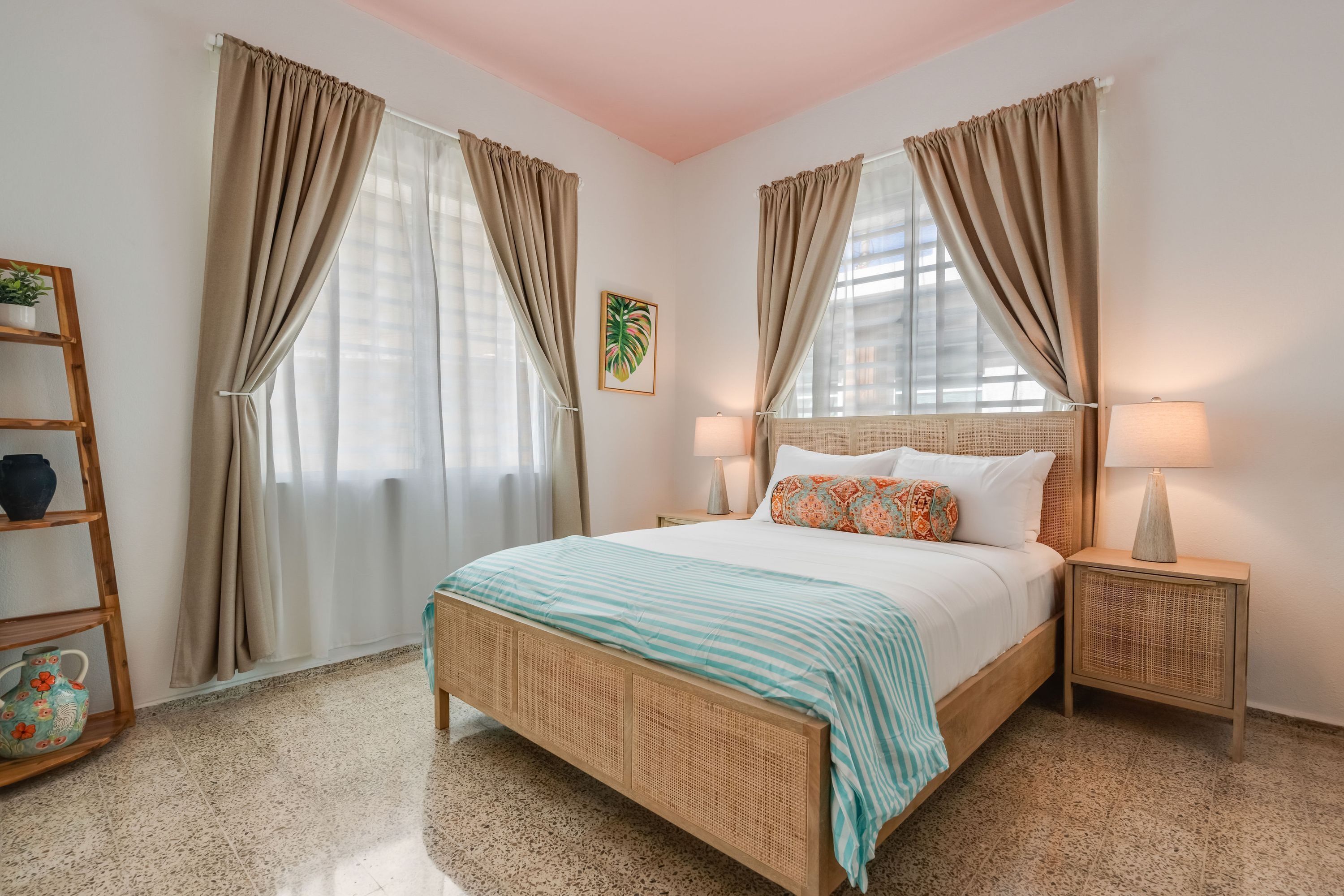 A bedroom with a bed, two bedside tables, a nightstand, a lamp, a shelf with decorative items, and a framed picture on the wall.