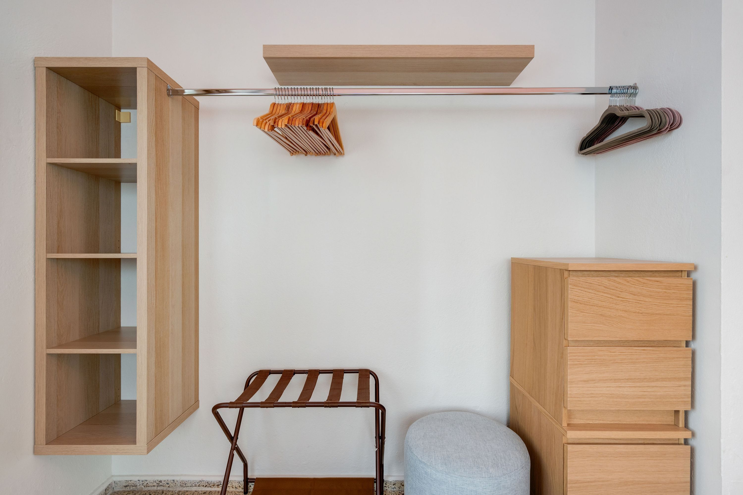 A room with a wooden wardrobe, a metal drying rack, and a small stool.