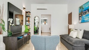 Un soggiorno moderno con un divano grigio, una poltrona blu, una televisione e un quadro raffigurante una spiaggia.