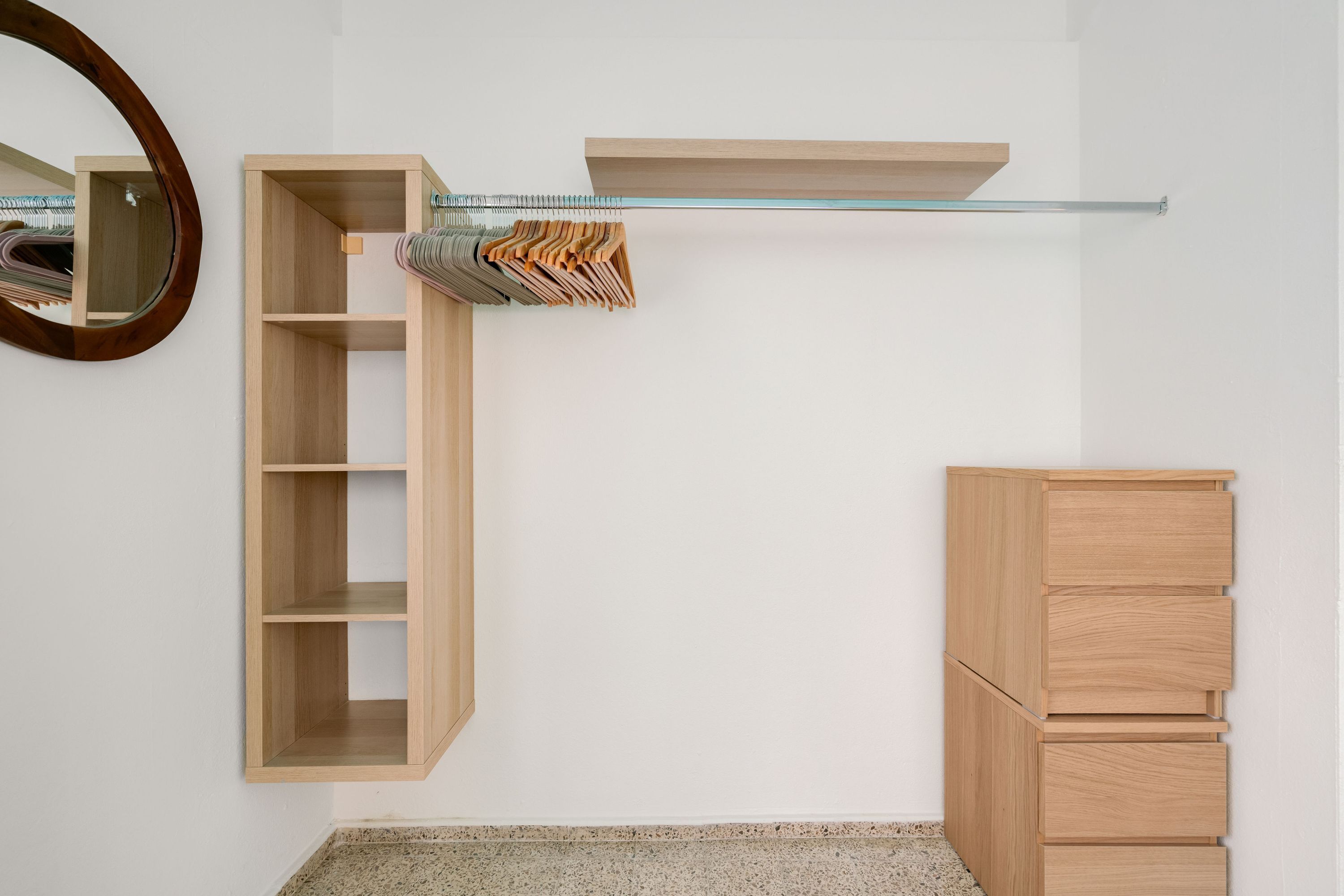 Een kamer met een houten garderobe, een spiegel en een plank met opgevouwen kleding.
