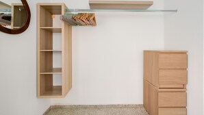Een kamer met een houten garderobe, een spiegel en een plank met opgevouwen kleding.
