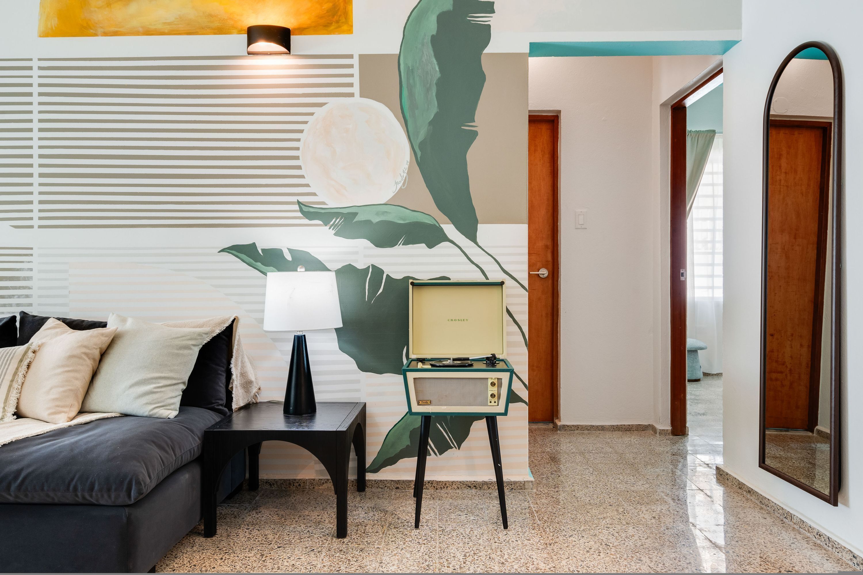 Una sala de estar moderna con un sofá, una mesita auxiliar, una radio antigua y un mural en la pared.