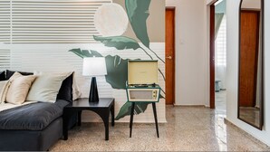 Een moderne woonkamer met een bank, een bijzettafeltje, een vintage radio en een muurschildering.