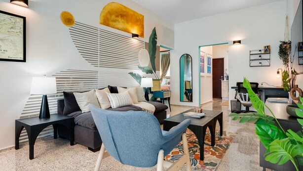 Een moderne woonkamer met een bank, fauteuil, salontafel en decoratieve planten.