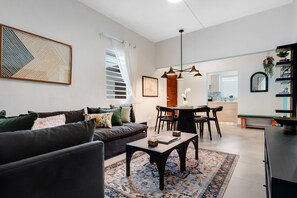 A modern living room with a dark sofa, a coffee table, and a dining area with a wooden table and chairs. - Stylish Apartment in Condado (San Juan)