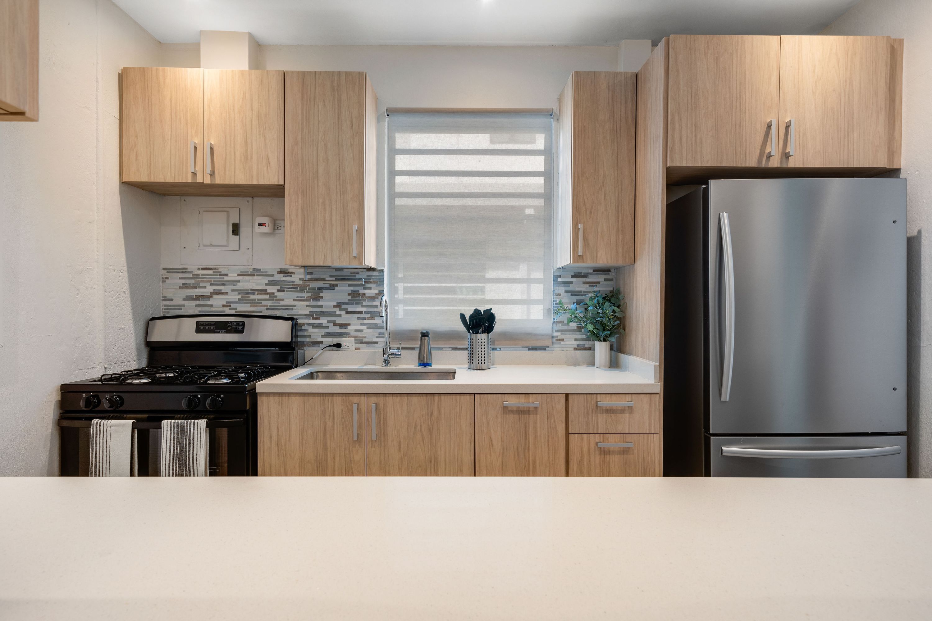 A modern kitchen with wooden cabinets, a stainless steel refrigerator, a gas stove, and a tiled backsplash.