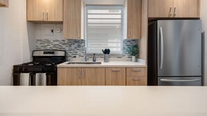 A modern kitchen with wooden cabinets, a stainless steel refrigerator, a gas stove, and a tiled backsplash. - Stylish Apartment in Condado (San Juan)