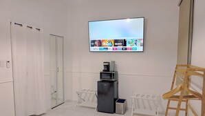 Ein modernes Hotelzimmer mit Flachbildfernseher, der Streaming-Dienste anzeigt, einer Minibar, einer Holzleiter und einer Duschkabine aus Glas.