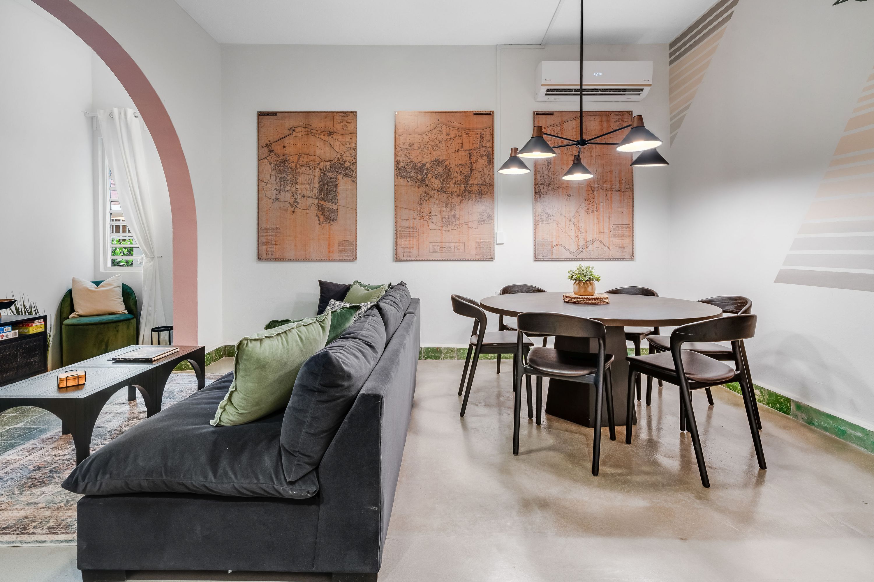 A modern living room with a black sofa, a dining table with chairs, and large wooden maps on the wall.