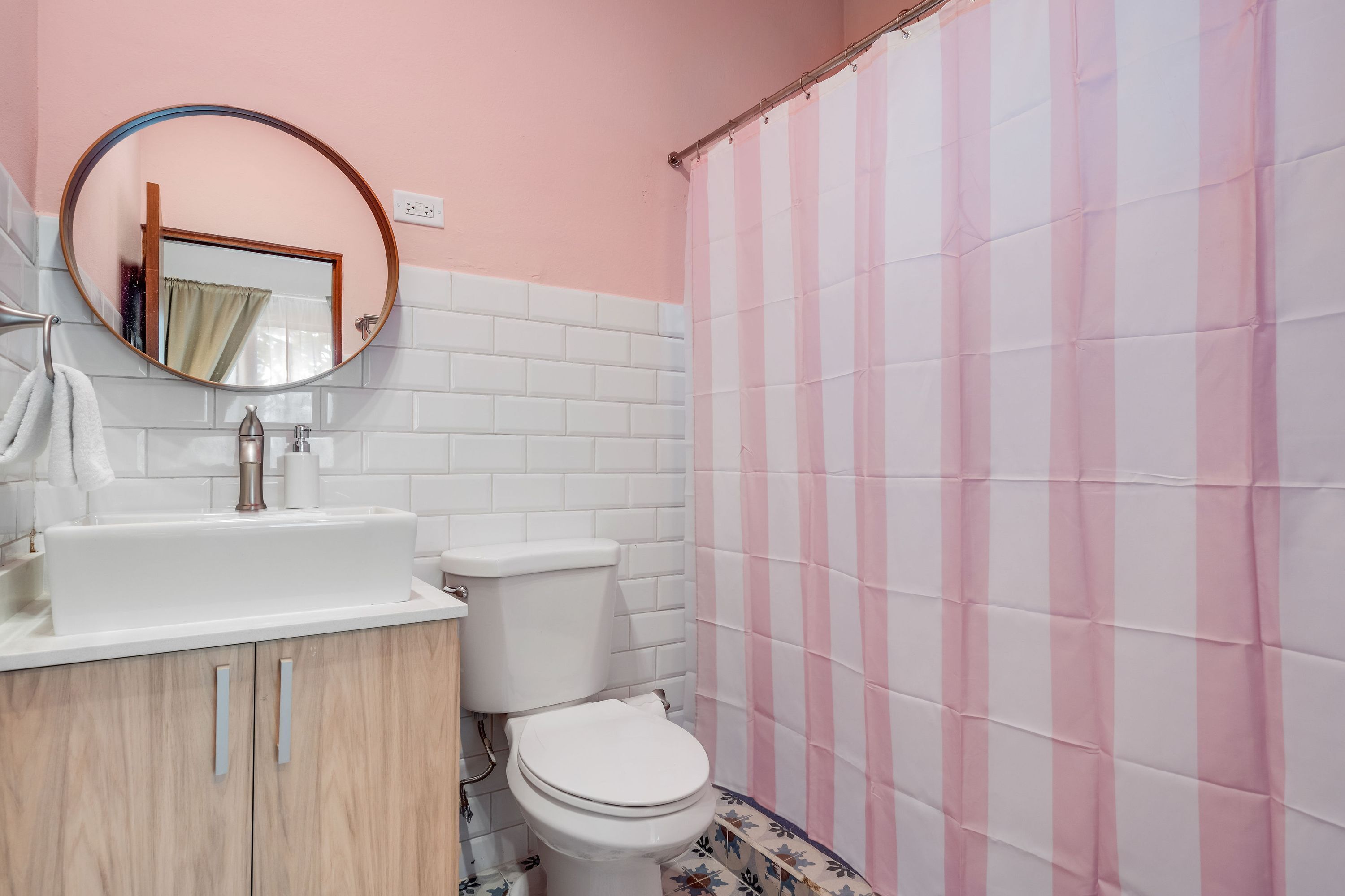 A bathroom with a white sink, toilet, and pink-striped shower curtain.
