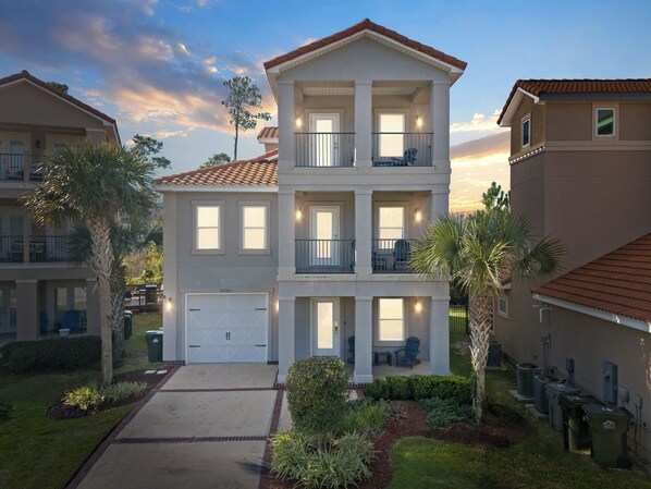 A multi-story residential building with a garage, balconies, and a well-maintained garden. - Warm Winter Escape, Spacious 4BR Home, Pool, Walk to the Beach! (Pensacola)