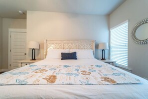 Une chambre à coucher avec un grand lit, deux tables de chevet avec des lampes, une porte et une fenêtre avec des stores.