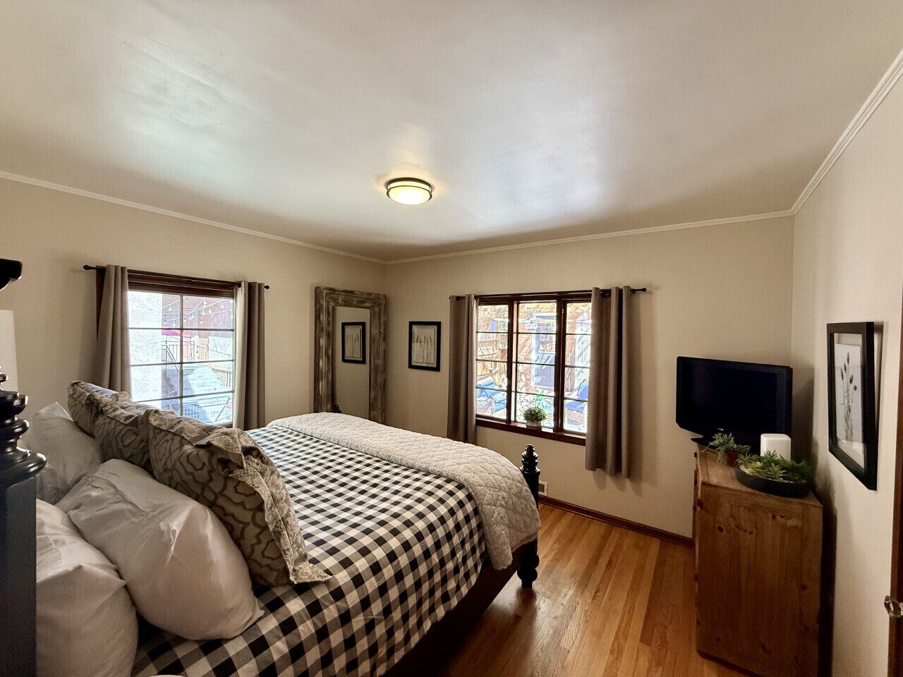 Una camera da letto con un letto, due finestre, un televisore su un mobile in legno e quadri appesi al muro.