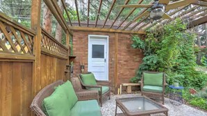 Eine überdachte Terrasse mit Korbmöbeln, einem Glastisch und einer Tür zu einem Innenbereich.