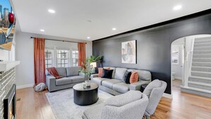 Una sala de estar moderna con chimenea, sofás grises, una mesa de centro y un ventanal con cortinas.