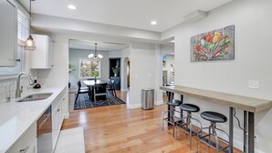 Una cocina moderna con armarios blancos, un lavamanos de acero inoxidable y una zona de comedor de madera con alfombra negra.