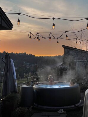 Un bain à remous dans un cadre extérieur rustique, illuminé par des guirlandes lumineuses suspendues au-dessus.