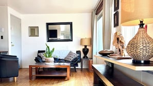 A modern living room with a wooden floor, a black sofa, a coffee table, and a lamp. - Sunset Ridge, Near Downtown, Hot tub, Outdoor Living, all with Panoramic View,  (Spokane)