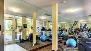 Een sportschool met trainingsapparatuur, grote spiegels en uitzicht op het buiten.