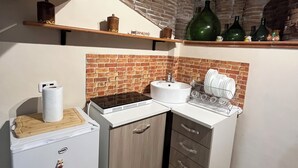 Eine kompakte Küche mit Kühlschrank, Spüle und Herd. Über der Arbeitsplatte befinden sich Regale mit verschiedenen Küchenutensilien.