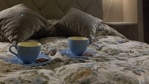 Ein Bett mit blumigem Bettzeug, zwei Kissen und ein Nachttisch mit Tasse und Untertasse.