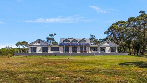 A modern two-story house with a flat roof and large windows, surrounded by a grassy lawn and trees. - Peninsula at Metung House | Boat Access Only Getaway (Boole Poole)