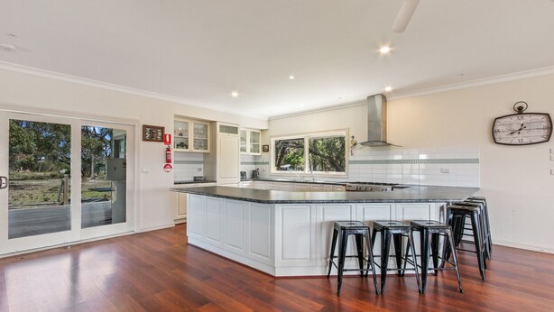 A modern kitchen with a large island, bar stools, and a clock on the wall. - Peninsula at Metung House | Boat Access Only Getaway (Boole Poole)