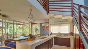 A modern kitchen with a central island, wooden cabinets, and a view of the outdoors through large windows.