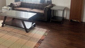 A living room with a brown leather sofa, a coffee table, a small side table, and a wooden cabinet. - Charming bungalow with AC and WiFi in a private rural part of Billings.  (Billings)