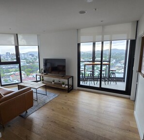 Un salon moderne doté d’un grand téléviseur, d’un plancher en bois, d’un canapé et d’un balcon avec une table et des chaises.
