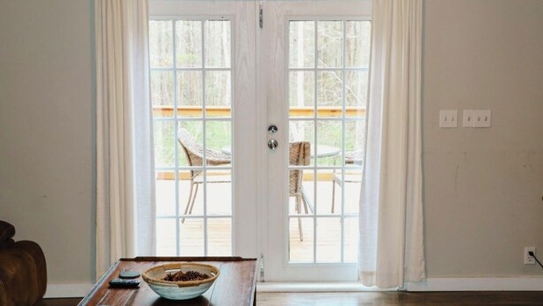 Quarto com mesa de madeira, uma tigela de grãos de café e vista para um deque externo com cadeiras.