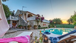 A stone house with a pool, lounge chairs, and a table with drinks and flowers. - Discover peace at Villa Kyklamino – your perfect Paxos escape (Gaios)