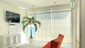 A modern living room with a large window, a potted palm tree, a red sofa, and a flat-screen TV mounted on the wall. - Modern Beachfront Luxury in Monrovia  (Monrovia)