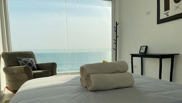 A bedroom with a large bed, a chair, a small table, and a view of the ocean. - Modern Beachfront Luxury in Monrovia  (Monrovia)