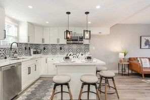 Una cocina moderna con armarios blancos, salpicadero con diseño blanco y negro, electrodomésticos de acero inoxidable e una isla central con taburetes.