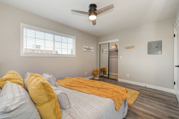 A bedroom with a bed, a ceiling fan, a window, a door, and a mirror.