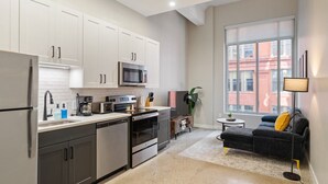 A modern kitchen with white cabinets, a microwave, and a stove. There is a dining area with a black sofa and a small table. - 2Bedroom, Near Over theRhine & Fountain Sq. + wifi (Cincinnati)