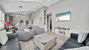 Un salon spacieux avec un grand canapé d’angle gris, une table basse et un téléviseur fixé au mur.